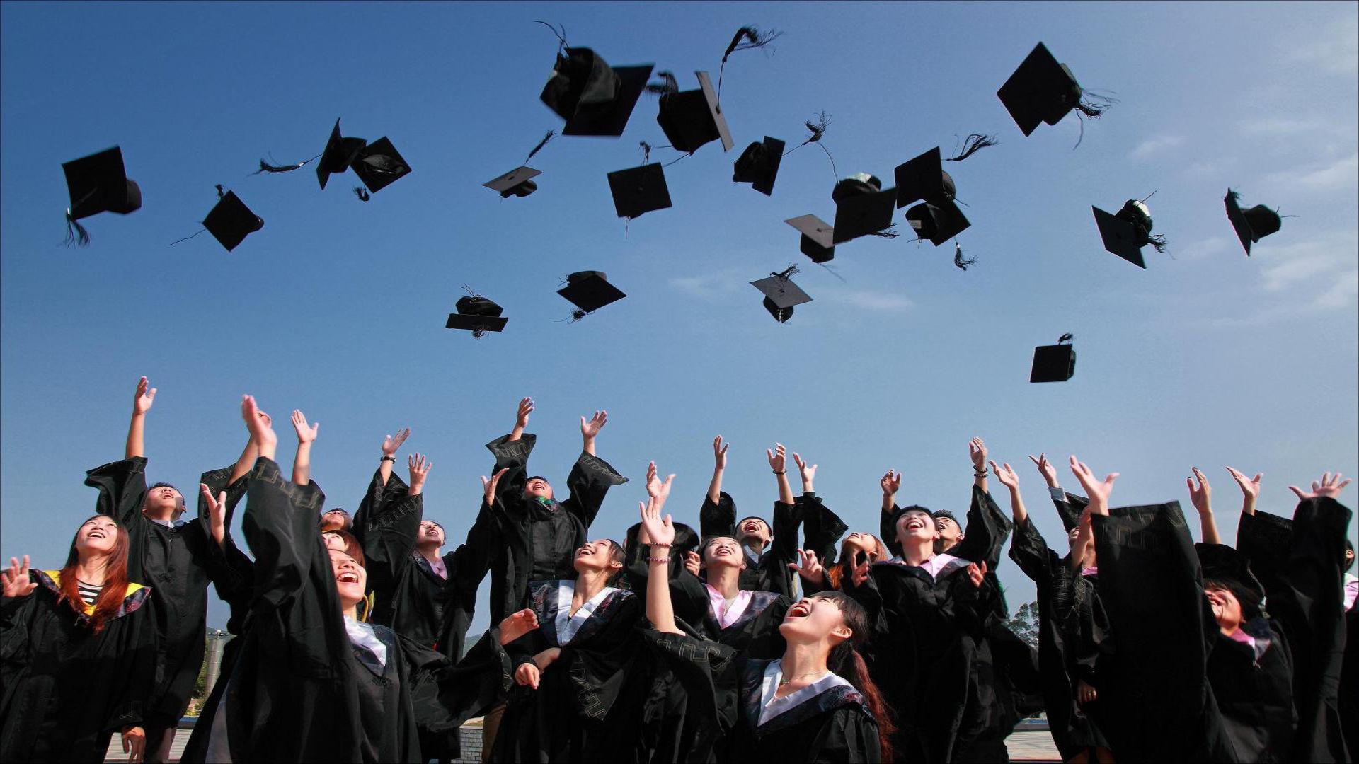 Foto de formandos arremessando chapéus de formatura